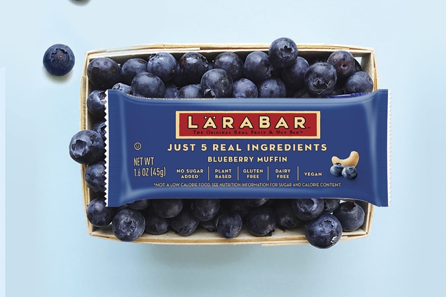 A blueberry Larabar in its package on top of a fruit basket full of blueberries